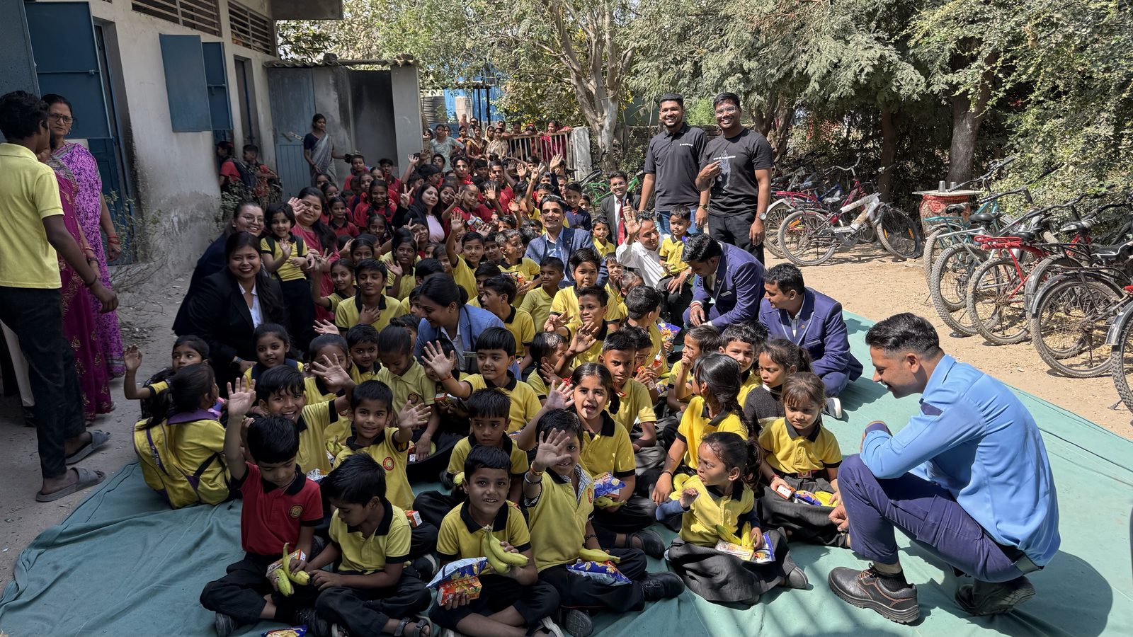 A large group of students seated outdoors in a school yard during a programme visit.